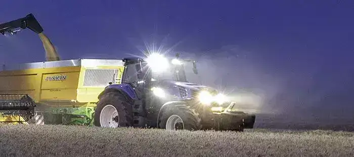 En blå New Holland T8 Genesis traktor som arbeider på åkeren om natten.