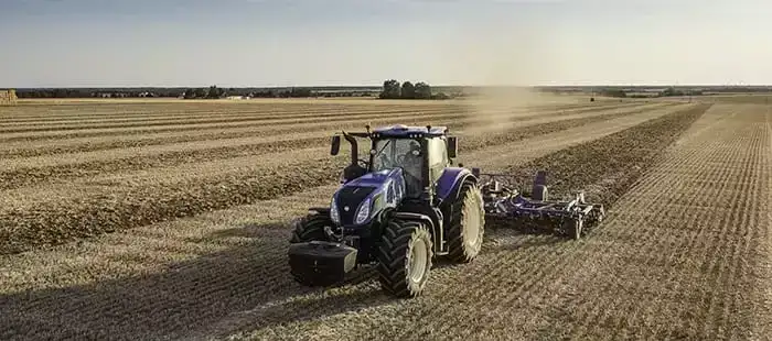 Blå New Holland T8 Genesis traktor i arbeid på en stor, åpen åker.