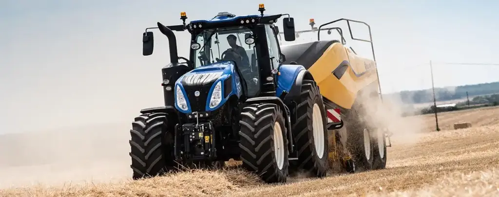 Blå New Holland T8 Genesis traktor i arbeid på en tørr åker om sommeren.