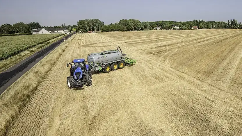 En blå New Holland T8 Genesis traktor med Joskin gjødselvogn på et gult jorde.