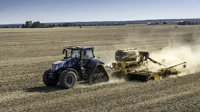 En blå New Holland T8 Genesis traktor arbeider på en tørr åker.