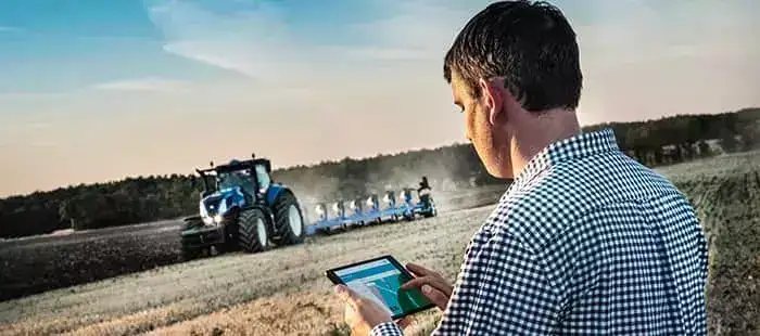En mann styrer en New Holland T8 Genesis traktor på åkeren med et nettbrett.