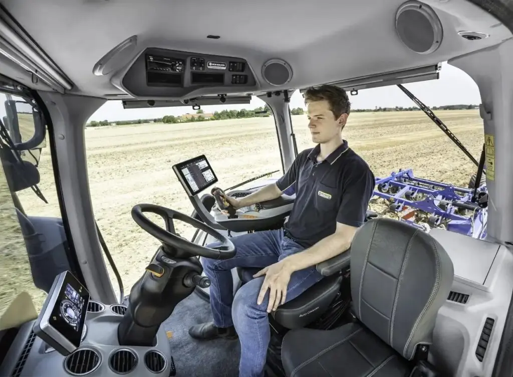 Førerhuset til en New Holland T8 Genesis traktor med en sjåfør som betjener kontrollene.