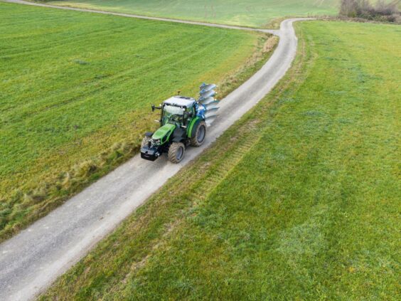 En grønn Deutz-Fahr Series 5D TTV traktor som kjører på en vei gjennom grønne marker.