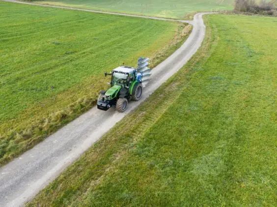 En grønn Deutz-Fahr Series 5D TTV traktor som kjører på en vei gjennom grønne marker.