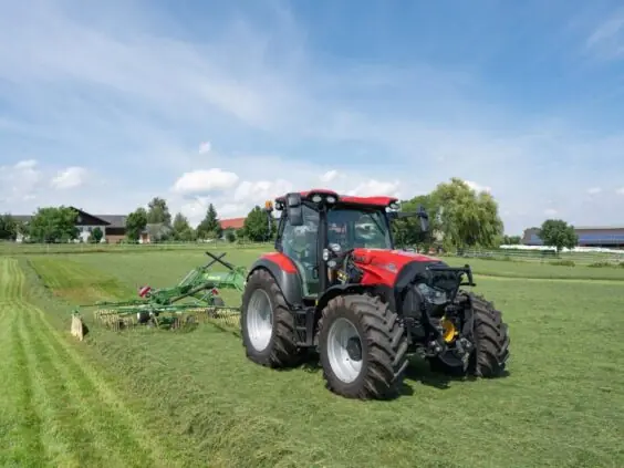 Rød Case IH traktor fra Vestrum-serien som bruker høyrive på en grønn mark.