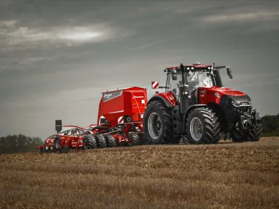 Rød traktor fra Magnum-serien med Kverneland såmaskin på en stubbmark under overskyet himmel.