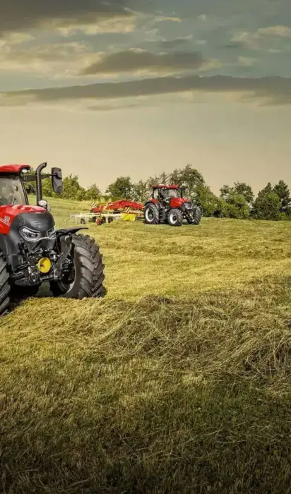 Rød Case IH traktor som samler høy på en åker under en dramatisk himmel.