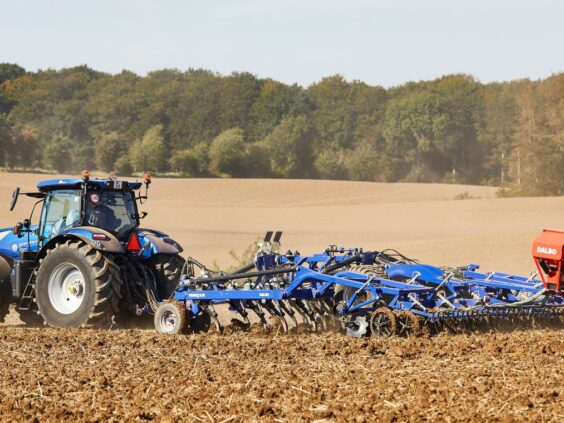 En blå traktor som trekker en DALBO Trimax Slept (Bugseret) stubbharv på et jorde.