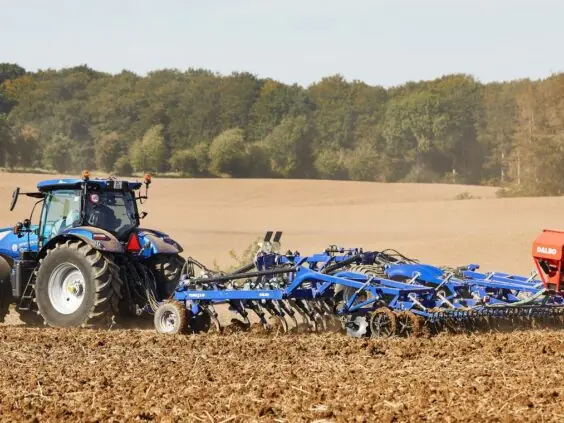 En blå traktor som trekker en DALBO Trimax Slept (Bugseret) stubbharv på et jorde.