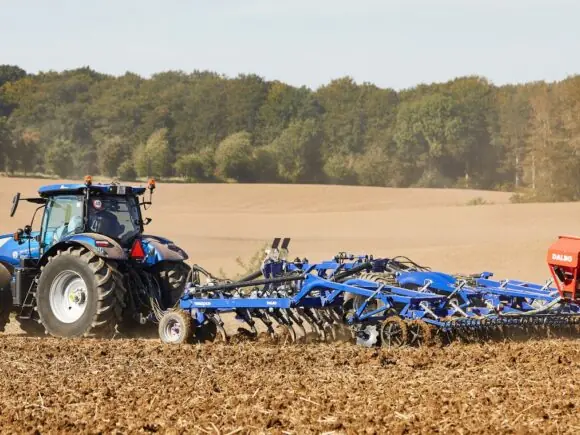 En blå traktor som trekker en DALBO Trimax Slept (Bugseret) stubbharv på et jorde.