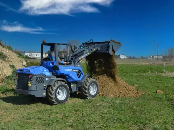 En blå MultiOne 11-serie kompaktlaster som dumper jord på en grønn slette.