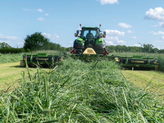En grønn traktor i arbeid på feltet med en KRONE EasyCut B slåmaskin.