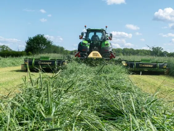 En grønn traktor i arbeid på feltet med en KRONE EasyCut B slåmaskin.