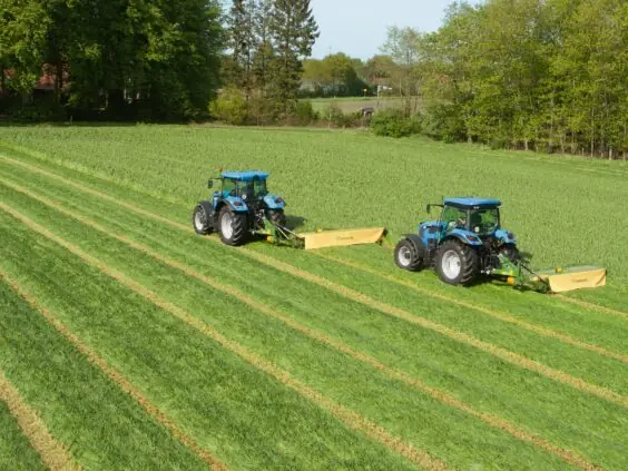Blå traktorer klipper gress på et jorde med Krone ActiveMow slåmaskin.