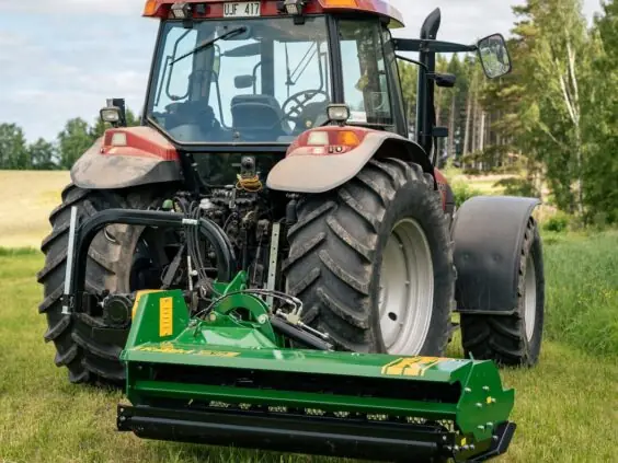En rød traktor med en grønn kantklipper montert bak på et gressfelt.