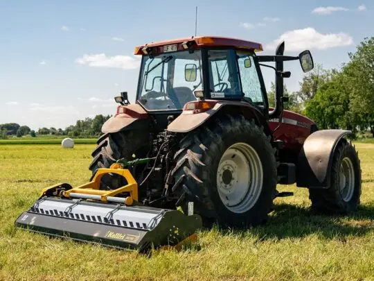 En rød traktor på en grønn eng med en Kellfri vertikalklipper montert bak.