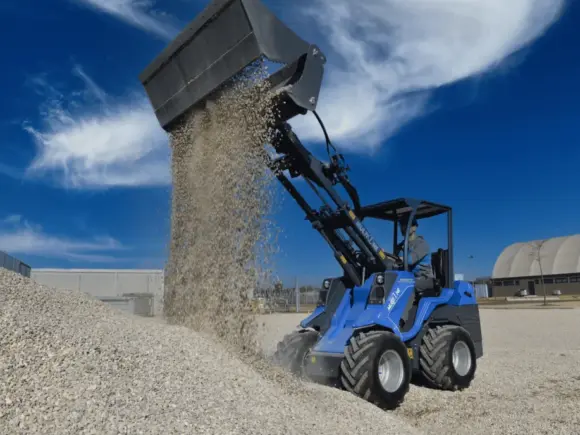 En blå MultiOne 5.3 minilaster som tipper grus på en haug under en blå himmel.