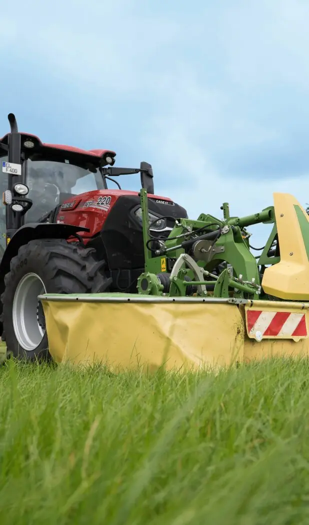 Rød traktor med Krone slåmaskin og tilhenger i arbeid på en grønn eng.