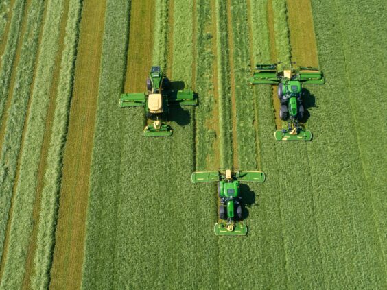 Tre traktorer i arbeid på et grønt jorde med KRONE EasyCut B slåmaskin.