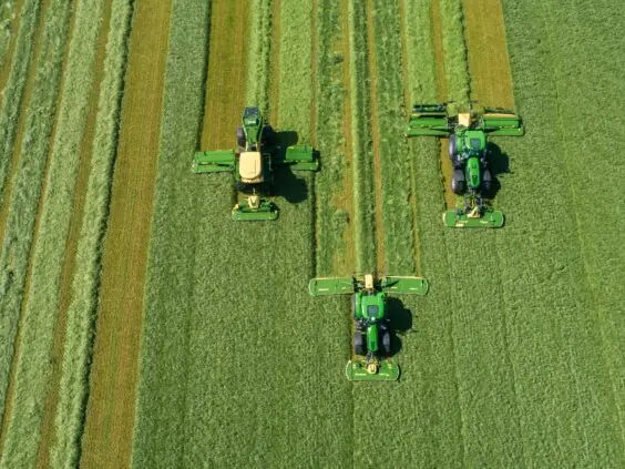 Tre traktorer i arbeid på et grønt jorde med KRONE EasyCut B slåmaskin.