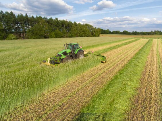 Grønn traktor i arbeid på gressfelt med en KRONE EasyCut B slåmaskin.