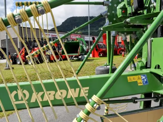 Grønn Krone-rive utstilt sammen med andre brukte landbruksmaskiner og redskap utendørs.