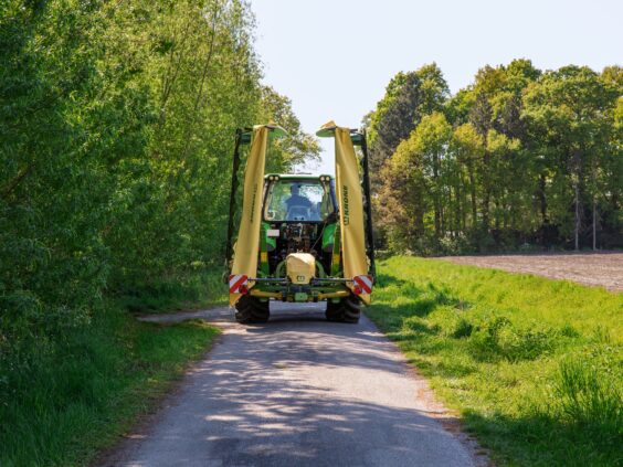 Grønn traktor med sammenslått KRONE EasyCut B slåmaskin på en landevei.