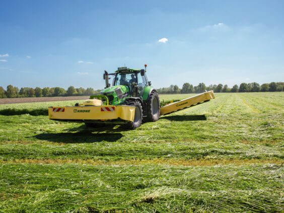 Grønn traktor på gressfelt utstyrt med KRONE EasyCut B slåmaskin.
