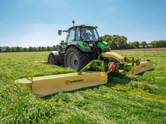 En grønn traktor i arbeid på feltet med en KRONE EasyCut B slåmaskin.