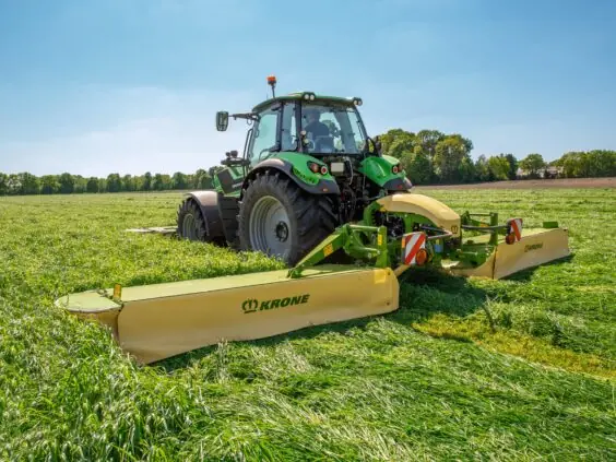 En grønn traktor i arbeid på feltet med en KRONE EasyCut B slåmaskin.