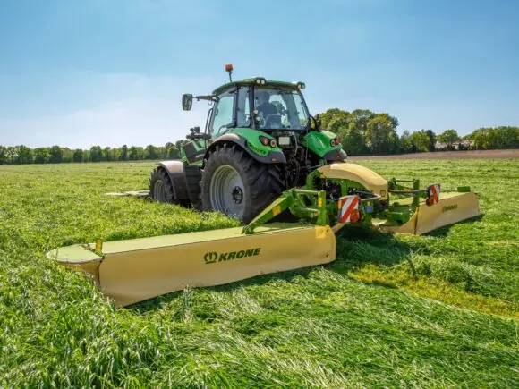 En grønn traktor i arbeid på feltet med en KRONE EasyCut B slåmaskin.