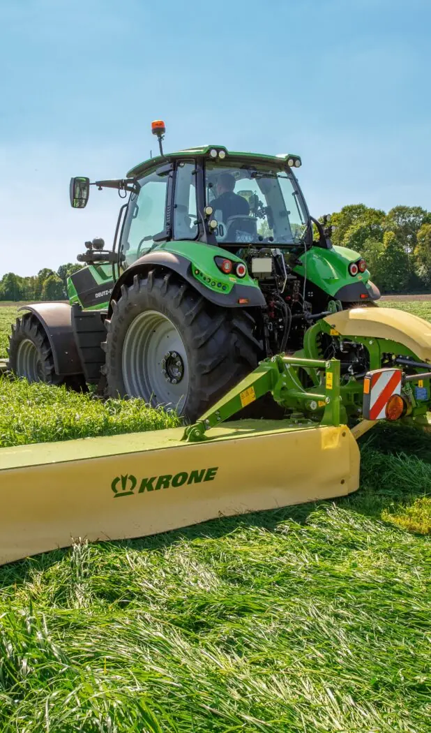 En grønn traktor i arbeid på feltet med en KRONE EasyCut B slåmaskin.