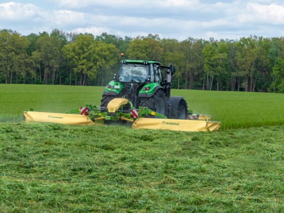 Grønn traktor som slår gress på en åker med KRONE EasyCut B slåmaskin.