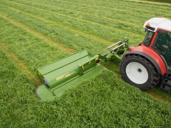 En rød traktor med Krone EasyCut R slåmaskin i et grønt gressfelt.