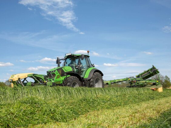 Grønn traktor i arbeid på feltet med en KRONE EasyCut TS/TC slåmaskin.