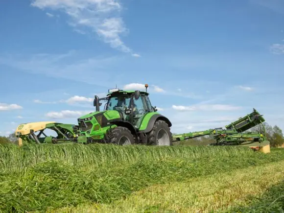 Grønn traktor i arbeid på feltet med en KRONE EasyCut TS/TC slåmaskin.