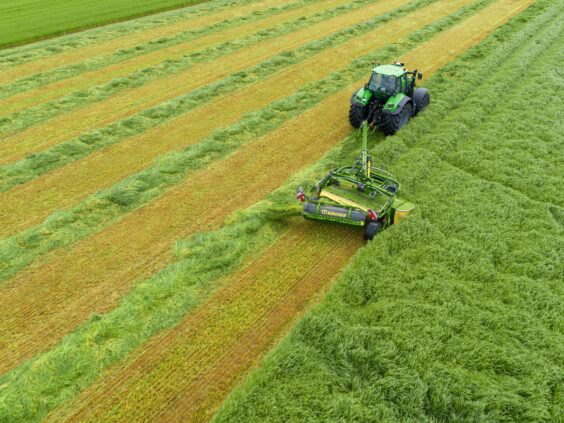 En grønn traktor i arbeid på feltet med en KRONE EasyCut TS/TC slåmaskin.