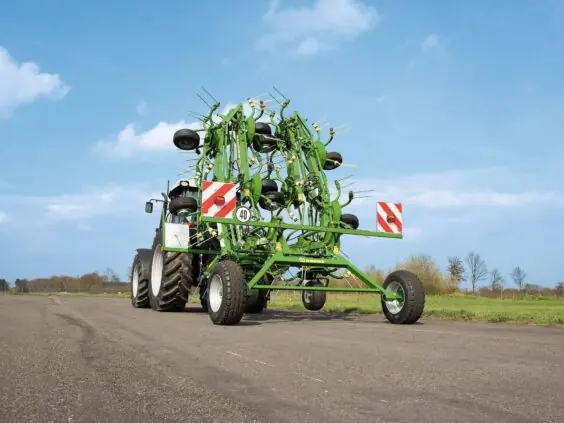 En Krone KWT høyvender foldet sammen og slept av en traktor på vei.