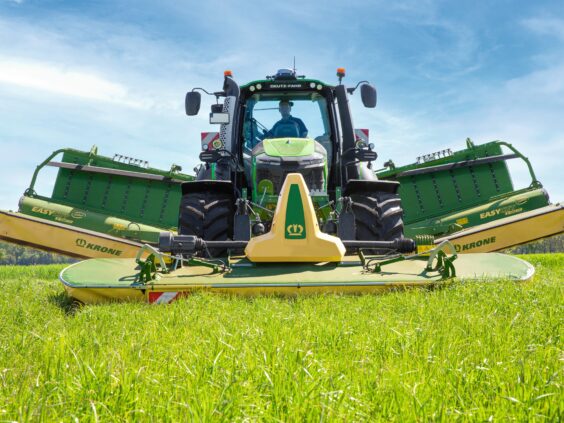 En Deutz-Fahr traktor på en grønn åker med en KRONE EasyCut B slåmaskin.