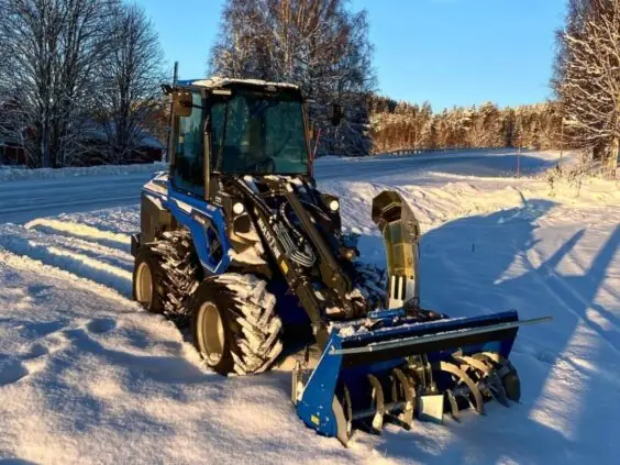 Blå MultiOne 8-serie kompaktlaster med snøfreser i et vakkert, snødekket vinterlandskap.