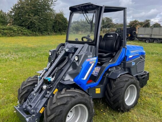 Blå MultiOne 8-serie kompaktlaster parkert på en grønn gressplen under en overskyet himmel.