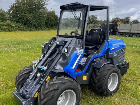 Blå MultiOne 8-serie kompaktlaster parkert på en grønn gressplen under en overskyet himmel.