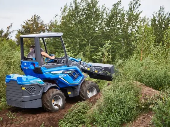 Blå MultiOne EZ-serie elektrisk kompaktlaster i arbeid på en jordhaug ute.