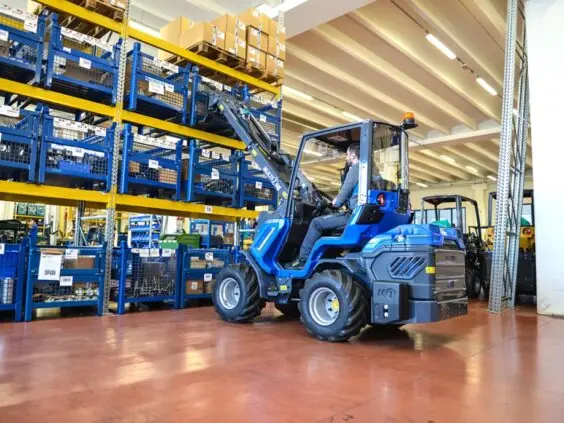En blå MultiOne EZ-serie elektrisk kompaktlaster i arbeid på et høytlager.