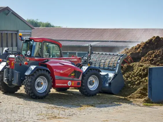 Rød Weidemann teleskoplaster T7042 i arbeid ved en fôrhaug på en gård.