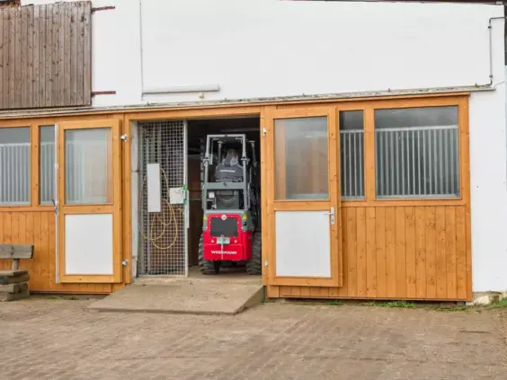 En rød Weidemann Hoftrac 1140 minilaster kjører inn i en stall.