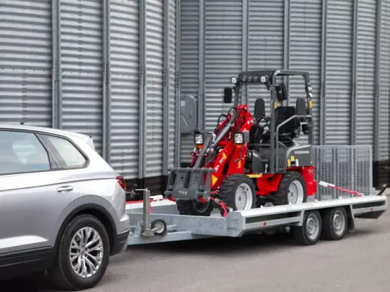 En rød Weidemann Hoftrac 1140 minilaster på tilhenger bak en sølvfarget SUV.