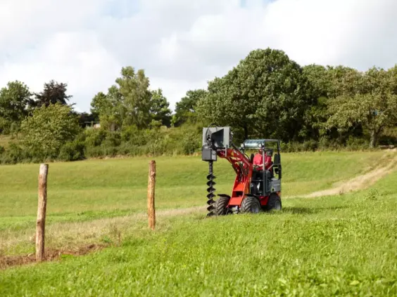 Weidemann Hoftrac 1140 Basic Line minilaster med jordbor i en grønn eng.