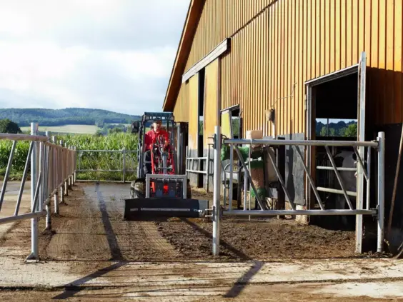 En rød Weidemann Hoftrac 1140 Basic Line minilaster i arbeid på en gård.